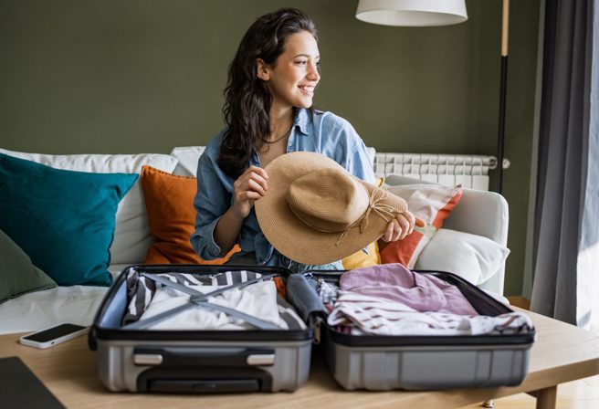 A woman smiles while packing her suitcase for a trip.
